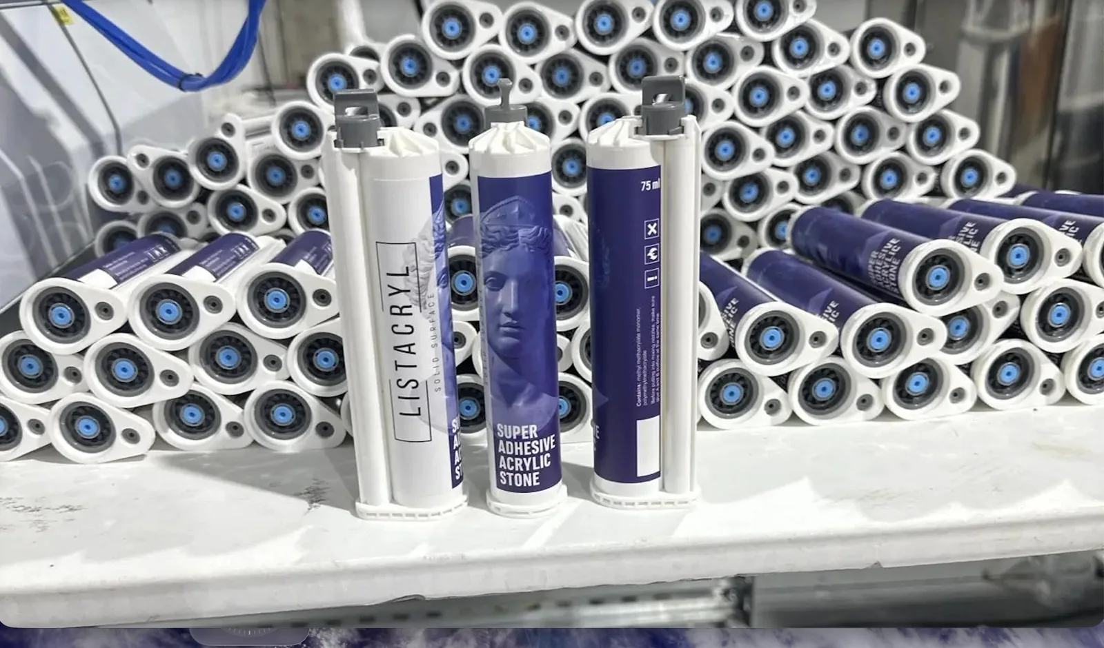 Три картриджа клея LISTACRYL Super Adhesive Acrylic Stone на столе перед штабелем готовой партии